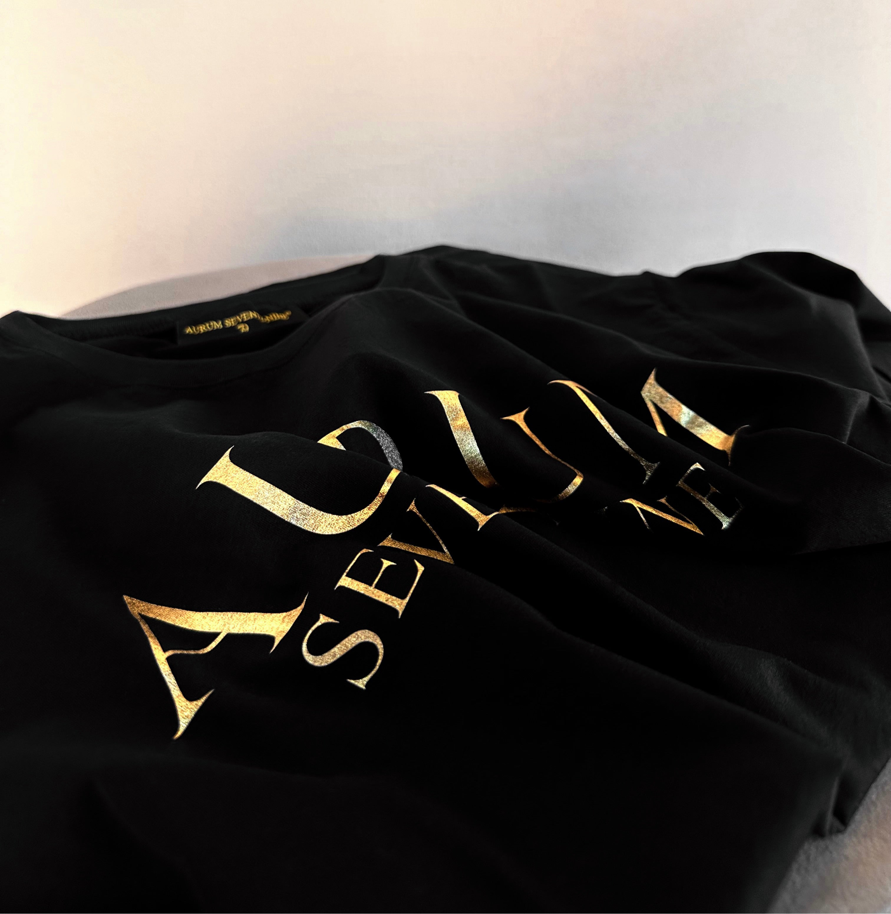 Aurum Seventy-nine: Foto vista dall'alto della T-shirt Round Neck Aurum Classic Black, con focus sul logo dorato al centro del petto.